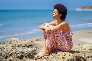 africano americano turista sentado em pedra e respiração fresco mar ar foto
