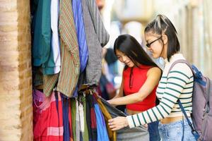 fêmea turistas escolhendo roupas dentro rua mercado foto