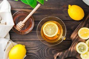 uma copo do chá com uma fatia do limão e uma tigela do querida em uma de madeira mesa. Vitamina orgânico nutrição. topo Visão foto