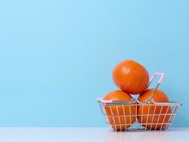maduro mandarinas dentro uma miniatura metal compras carrinho em uma azul fundo, citrino preço aumentar conceito