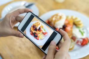 restaurante proprietário leva uma cenário do a Comida em a mesa com uma Smartphone para postar em uma local na rede Internet. conectados Comida entrega, encomenda serviço, influenciador, análise, social meios de comunicação, compartilhar, marketing, interesse foto