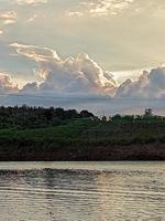 uma barco é dentro a água e a céu é azul e a água é calma. uma árvore dentro a primeiro plano com a Sol brilhando através a nuvens. a água é calma. foto