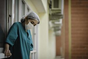 Enfermeira asiática deprimida cansada usa máscara facial uniforme azul senta-se no chão do hospital, jovem médica estressada pelo trabalho duro foto