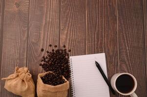 café, grãos de café e um caderno com uma caneta sobre uma mesa de madeira foto