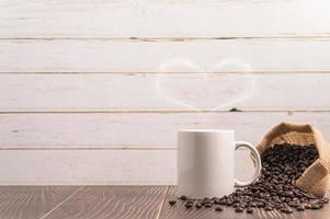 uma caneca de café fazendo vapor em forma de coração com um saco de grãos de café em uma mesa de madeira foto