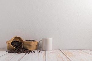 uma caneca de café e sacos de grãos de café em uma mesa de madeira foto