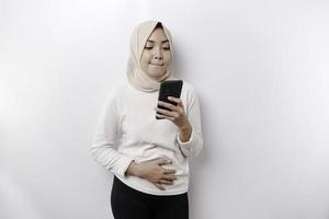 uma pensativo jovem ásia muçulmano mulher vestindo uma hijab e segurando dela queixo enquanto falando em a telefone isolado de uma branco fundo foto