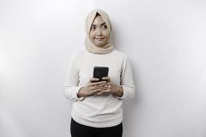 uma feliz ásia muçulmano mulher vestindo uma lenço de cabeça, segurando dela telefone, isolado de branco fundo foto