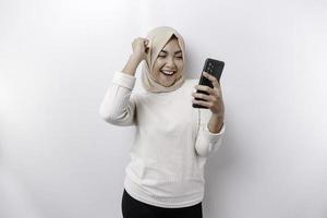 uma jovem ásia muçulmano mulher com uma feliz bem sucedido expressão vestindo uma hijab e segurando Smartphone isolado de branco fundo foto