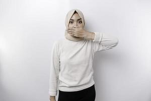 retrato do uma jovem ásia muçulmano mulher vestindo uma lenço de cabeça é contar estar quieto, calar com sério face, silêncio com dedo pressionado para lábios, isolado de branco fundo foto