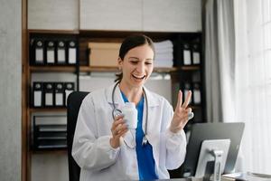 atraente fêmea médico falando enquanto explicando médico tratamento para paciente através uma vídeo ligar com computador portátil dentro escritório foto