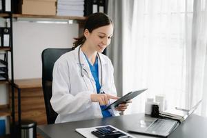 sorridente médico ou consultor sentado às uma escrivaninha dele pescoço olhando às a Câmera foto