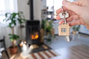 chave de casa com chaveiro no fundo da lareira fogão com fogo e lenha. lar aconchegante. construção, design, projeto, mudança para casa nova, hipoteca, aluguel e compra de imóveis foto