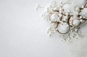ovos pintados de páscoa, flores e penas em um fundo branco texturizado foto