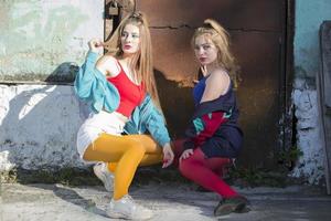 dois engraçado meninas dentro brilhante roupas dentro a estilo do a anos noventa estão sentado contra a fundo do uma oxidado porta. russo Vila garotas. foto