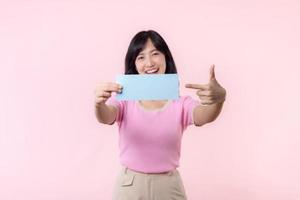 retrato feliz jovem mulher modelo segurando e mostrando em branco espaço papel para propaganda em formação mensagem poster com polegar acima ou ponto dedo gesto isolado em Rosa pastel estúdio fundo. foto