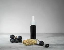 óleo de semente de uva em uma garrafa de vidro com uvas pretas frescas, óleo ou soro essencial para a pele, conceito de cosmético orgânico natural para cuidados de beleza foto