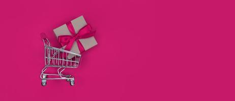 carrinho de supermercado e caixa de presente em um fundo rosa, conceito de compras