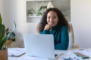 tiro do ásia sorridente o negócio mulher trabalhando com computador portátil enquanto olhando às Câmera dentro moderno comece escritório. foto