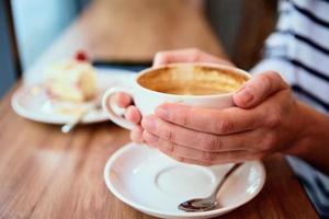 mulher ter café da manhã às cafeteria, aguarde café boné dentro mãos foto