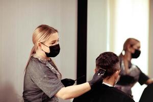uma cabeleireiro com segurança medidas para COVID-19, cortes uma homem dentro uma remédio mascarar, corte cabelo com uma médico mascarar e borracha luvas. foto