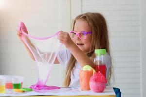 pequeno menina alongamento Rosa lodo para a lados. crianças mãos jogando lodo brinquedo. foto