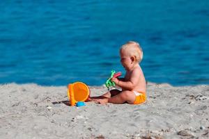criança pequena sentado em a de praia e jogando com plástico brinquedos dentro a areia. foto