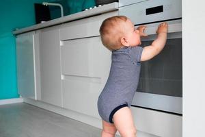 pequeno criança jogando com elétrico fogão dentro a cozinha. bebê segurança dentro cozinha foto