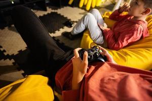 dois irmãos jogando vídeo jogos console, sentado em amarelo pufe dentro crianças jogar Centro. foto