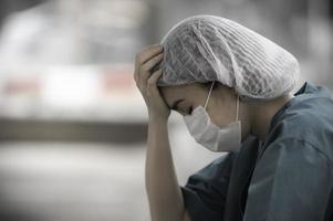 Enfermeira asiática deprimida cansada usa máscara facial uniforme azul senta-se no chão do hospital, jovem médica estressada pelo trabalho duro foto