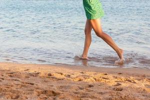lindo menina pernas corrida em a de praia. bonita menina caminhando em água foto