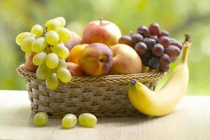fresco maduro maçãs, pêssegos, verde e azul uvas, bananas e Melancia dentro cesta. saudável Comida em mesa em desfocar outono fundo. foto