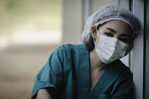 Enfermeira asiática deprimida cansada usa máscara facial uniforme azul senta-se no chão do hospital, jovem médica estressada pelo trabalho duro foto