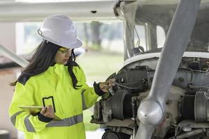 técnico consertando o motor do avião, engenharia aeroespacial feminina verificando motores de aeronaves, manutenção mecânica asiática inspeciona motor de avião foto