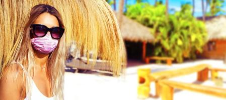 bela turista com máscara de vírus corona na praia foto