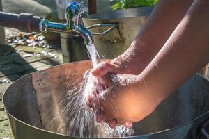 ásia Garoto lavando mãos em metal afundar, fechar acima do lavando mãos debaixo corrida água, limpeza higiene das mãos conceito. foto