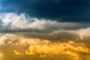 dramático azul nuvens de tempestade em topo e amarelo-dourado fofo nuvens iluminado de raios do Sol em abaixo. deslumbrante Visão natural meteorologia fundo foto