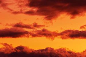 laranja nuvens brilhando de desaparecendo raios às pôr do sol flutuando através amarelo céu foto