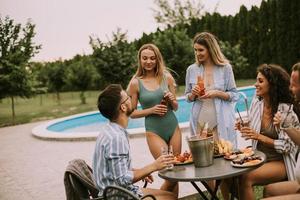 grupo de jovens torcendo com cidra à beira da piscina no jardim foto