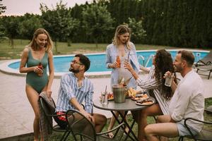 grupo de jovens torcendo com cidra à beira da piscina no jardim foto