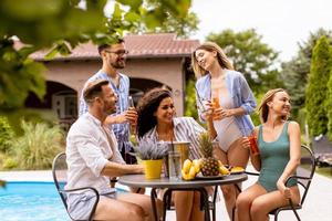 grupo de jovens torcendo com cidra à beira da piscina no jardim foto