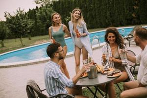 grupo de jovens torcendo com cidra à beira da piscina no jardim foto