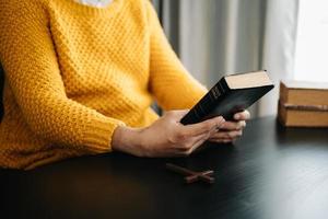 mãos juntas em oração a deus junto com a bíblia no conceito cristão e religião, mulher reza na bíblia na mesa de madeira foto