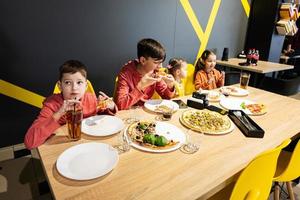 quatro crianças comendo italiano pizza dentro pizzaria. crianças comer às cafeteria. Garoto beber suco. foto