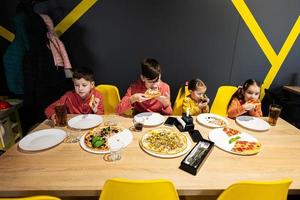 quatro crianças comendo italiano pizza dentro pizzaria. crianças comer às cafeteria. foto