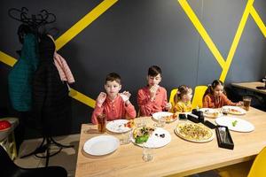 quatro crianças comendo italiano pizza dentro pizzaria. crianças comer às cafeteria. foto