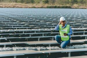 engenheiro inspetor segurando computador portátil e trabalhando dentro solar painéis poder plantar verificação fotovoltaico células e eletricidade Produção. foto