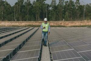 engenheiro inspetor segurando computador portátil e trabalhando dentro solar painéis poder plantar verificação fotovoltaico células e eletricidade Produção. foto