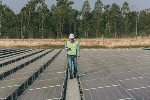 engenheiro inspetor segurando computador portátil e trabalhando dentro solar painéis poder plantar verificação fotovoltaico células e eletricidade Produção. foto