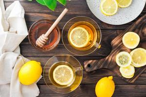dois copos do chá com limão, uma fatiado limão e uma tigela do querida em uma de madeira mesa. Vitamina orgânico nutrição. topo Visão foto